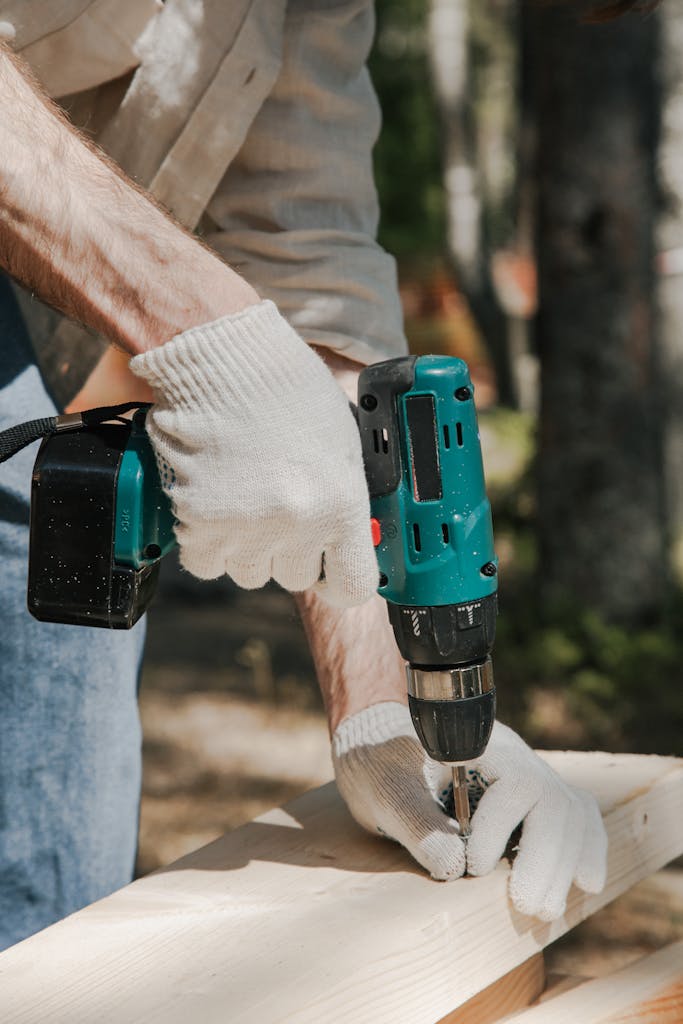 Person using Skil 20V cordless drill on outdoor woodworking project wearing gloves.