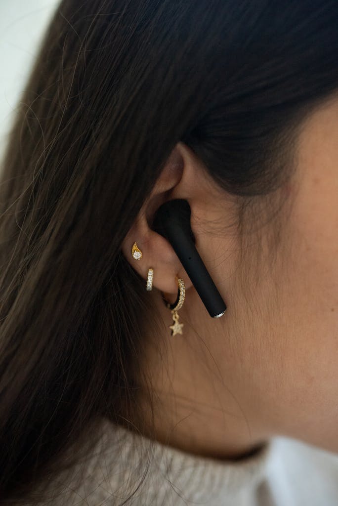 Close-up of a woman wearing JLab Go Air Pop black wireless earbuds and gold earrings