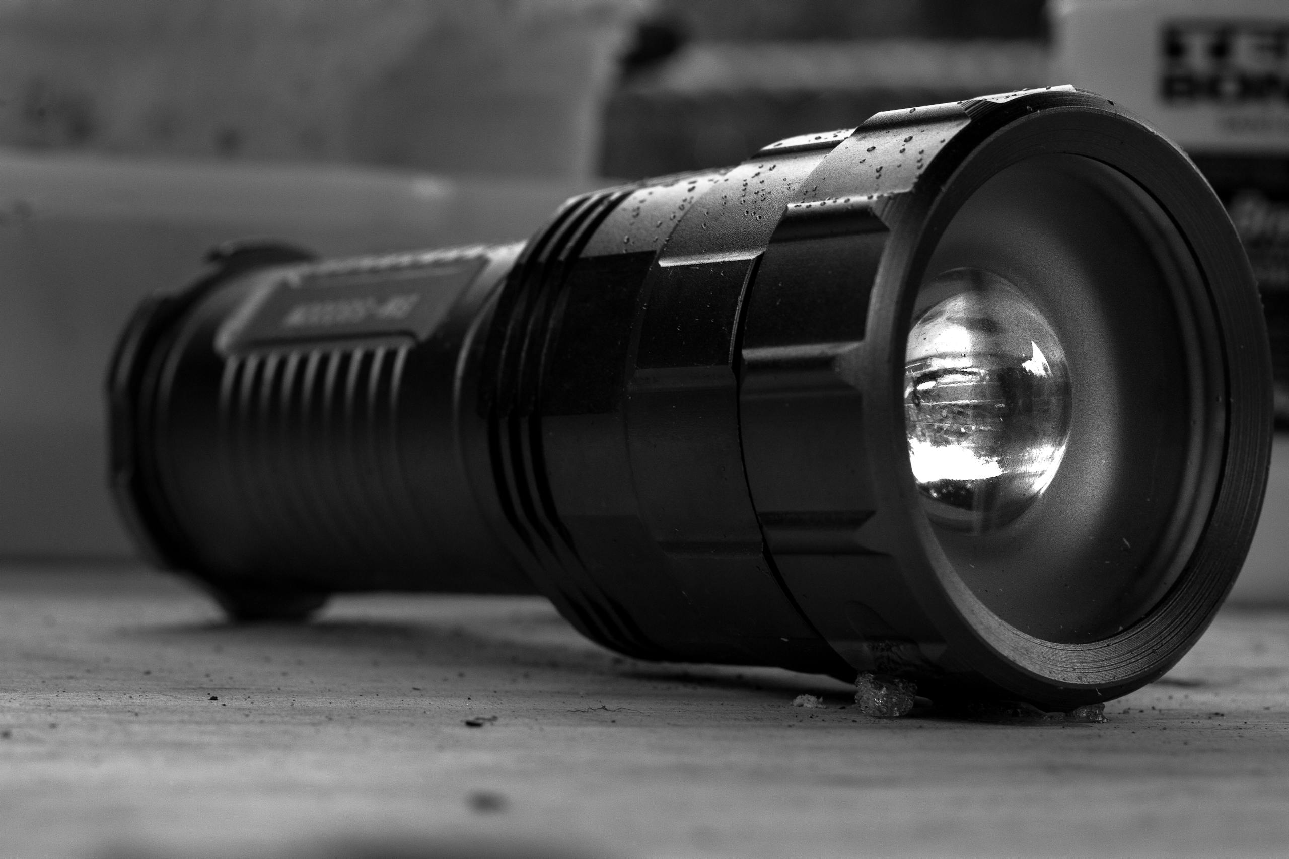 Detailed black and white photo of a flashlight on a surface, emphasizing texture.