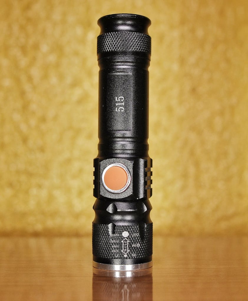 Detailed close-up of a black flashlight with orange button on a reflective surface.